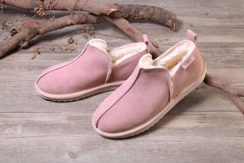Pink suede slip-on slippers with cozy shearling lining on rustic wood