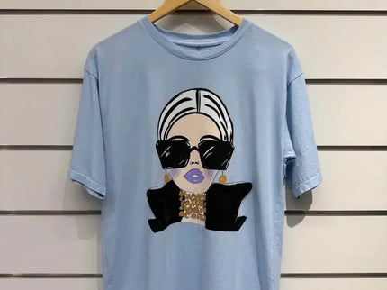Light blue graphic tee with stylish woman print, oversized sunglasses, and gold jewelry, modern fashion design