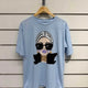 Light blue graphic tee with stylish woman print, oversized sunglasses, and gold jewelry, modern fashion design