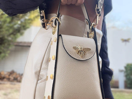Cream leather handbag with gold bee clasp, chain strap, and studded details, styled with navy sweater.