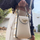 Cream leather handbag with gold bee clasp, chain strap, and studded details, styled with navy sweater.