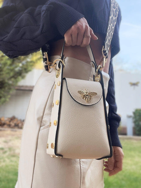 Cream leather handbag with gold bee clasp, chain strap, and studded details, styled with navy sweater.