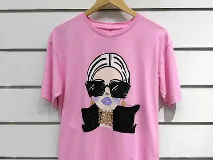 Pink graphic tee with stylish woman print, oversized sunglasses, and gold jewelry on white wall