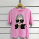 Pink graphic tee with stylish woman print, oversized sunglasses, and gold jewelry on white wall