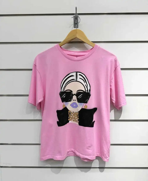 Pink graphic tee with stylish woman print, oversized sunglasses, and gold jewelry on white wall