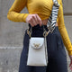 White leather crossbody bag with gold bee clasp and zebra strap, styled with yellow top and black pants